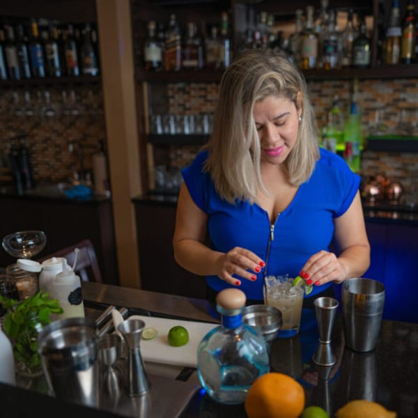 A bartender in a blue top garnishes a cocktail with a lime at Esposito's Pizza Bar.