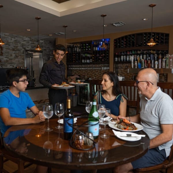 A waiter serves Italian dishes to a family of three at a round table in Esposito's Pizza Bar.