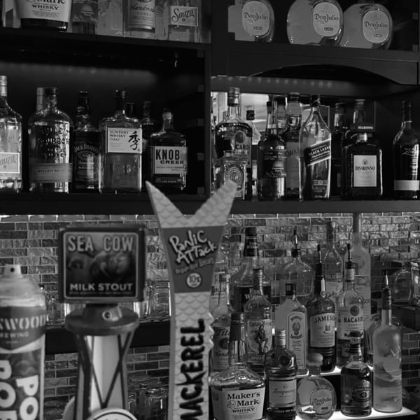 A black and white close-up of a bar with various liquor bottles and beer taps.