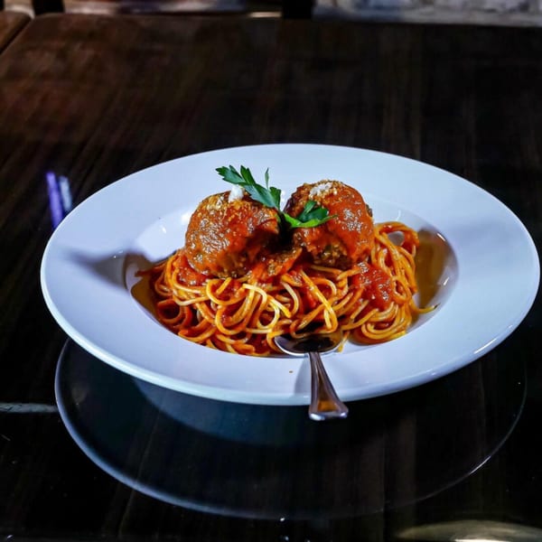 Esposito's spaghetti and meatballs, garnished with parsley and parmesan, on a white plate.