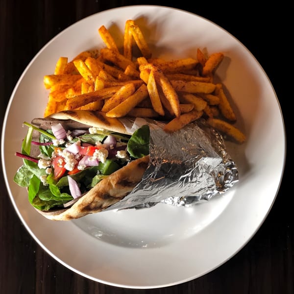 Grilled pita wrap with fresh greens, tomatoes, feta, and red onion, served with seasoned fries.