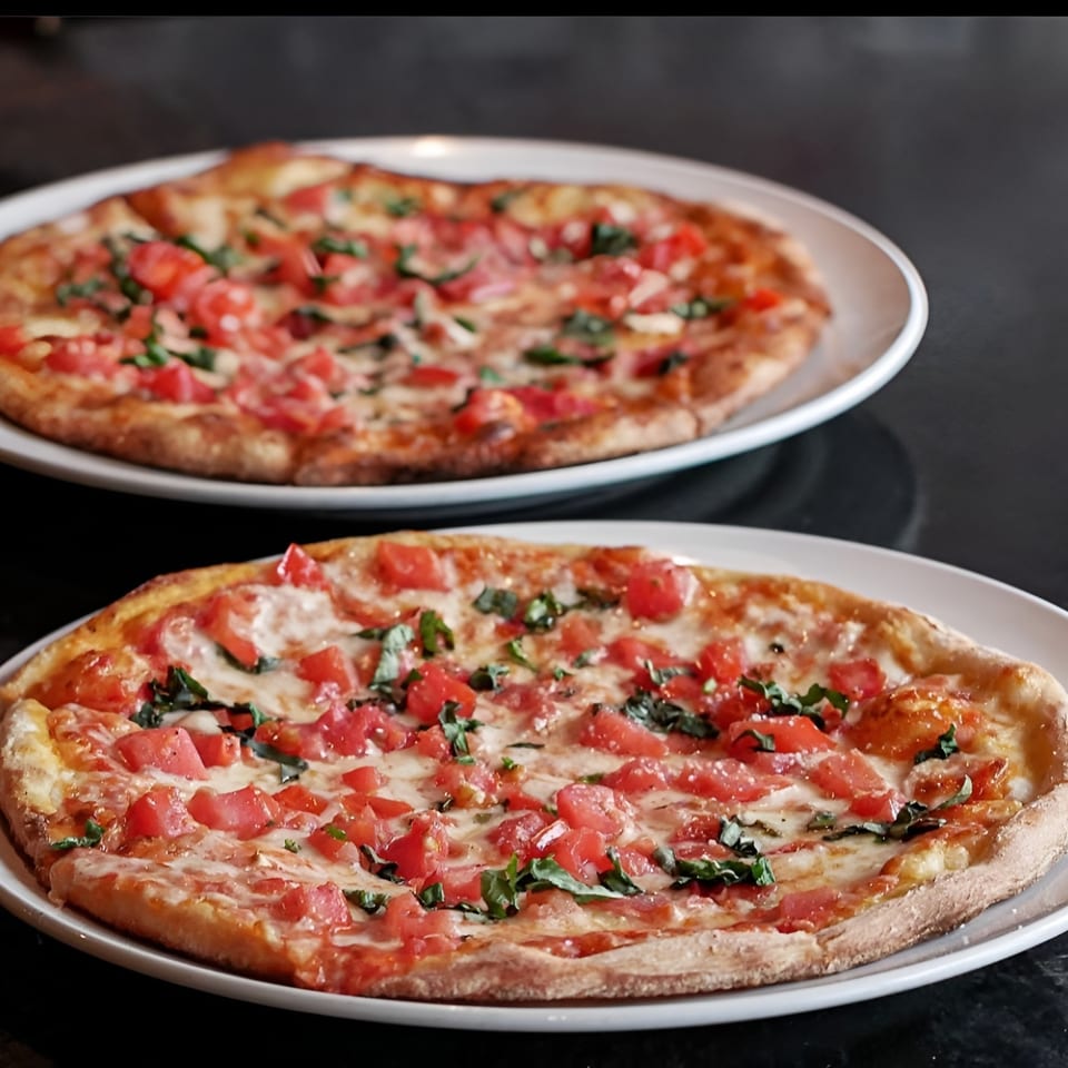 Two freshly baked Esposito's Pizza Bar Margherita pizzas with diced tomatoes and basil.