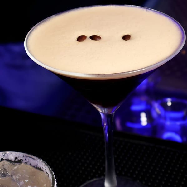 Espresso martini with coffee beans on top, against a dark background with blue lighting.