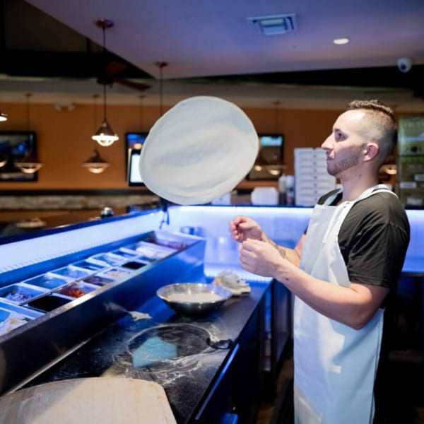 A chef in a white apron expertly tosses pizza dough high in the air at Esposito's.