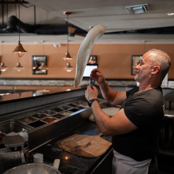 Esposito's Pizza Bar chef tossing pizza dough high in the air behind the counter.