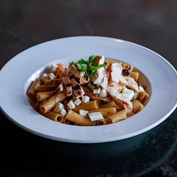 Esposito's rigatoni pasta with grilled chicken, feta cheese, and parsley in a white bowl.