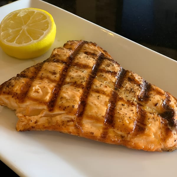 Grilled salmon fillet with grill marks and a lemon half on a white rectangular plate.
